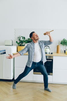 Joyful man singing into a wooden spoon in a modern kitchen setting.